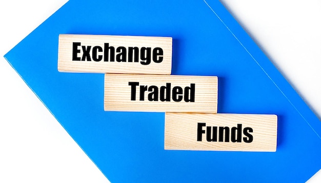 On a light gray background a blue notebook and three wooden blocks with the words ETF Exchange Traded Funds