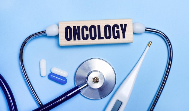 밝은 회색 배경에서 전자 온도계는 ONCOLOGY Medical 개념이 있는 나무 블록을 알약으로 만듭니다.