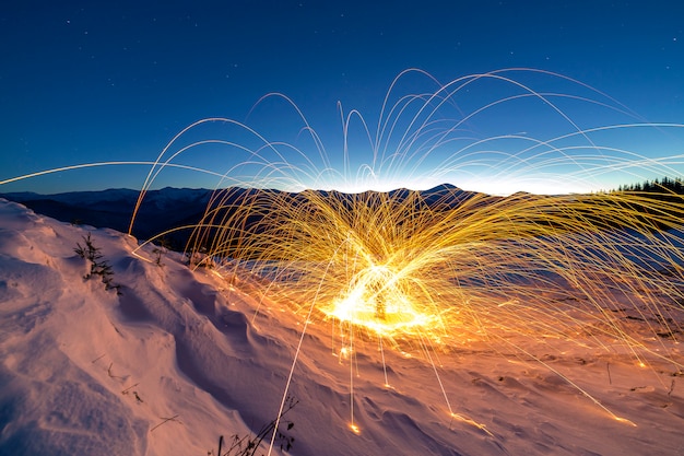Light painting art. Spinning steel wool in abstract circle, firework showers of bright yellow glowing sparkles on winter snowy valley on mountain ridge and blue night starry sky copy space .