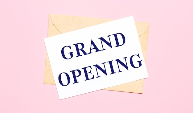 Photo on a light pink background - a craft envelope. it has a white sheet of paper that says grand opening