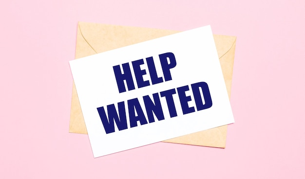 On a light pink background - a craft envelope. It has a white sheet of paper that says HELP WANTED