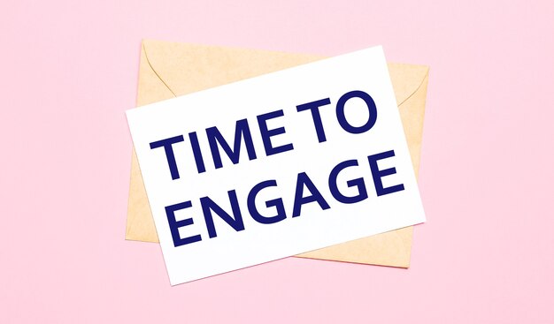 On a light pink background - a craft envelope. It has a white sheet of paper that says TIME TO ENGAGE.