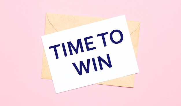 Photo on a light pink background - a craft envelope. it has a white sheet of paper that says time to win.