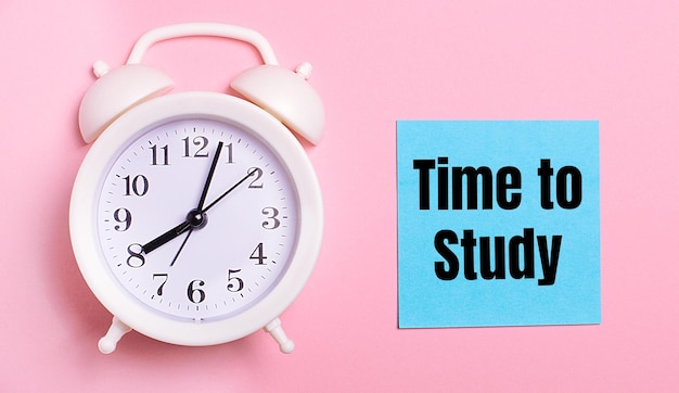 On a light pink background a white alarm clock and a blue sheet of paper with the text TIME TO STUDY