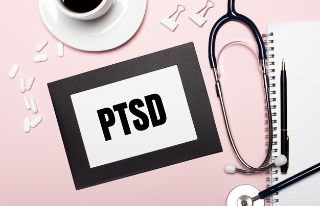 On a light pink surface a sheet of paper with the text PTSD. Medical concept