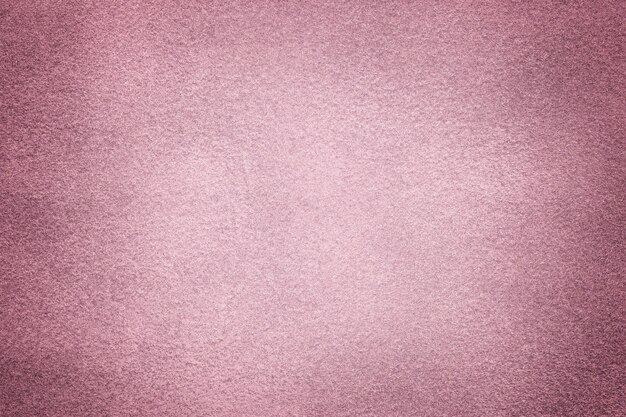 Light purple matte background of suede fabric with dark vignette, closeup. Velvet texture of seamless lilac textile with gradient, macro. Structure of pink felt canvas backdrop.