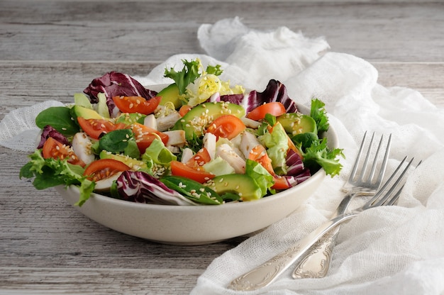 Photo light salad organic mix lettuce with tomatoes, avocado, slices of chicken breast, seasoned roasted sesame seeds.