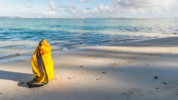 Photo light and shadow on sandy beach with yellow waterproof bag