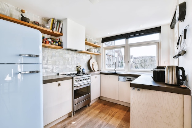 Light small home kitchen with wide window furnished with cupboards and shelves with appliances in modern urban apartment