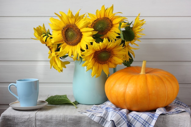 Natura morta leggera con un mazzo di girasoli e una zucca sul tavolo. raccolto, abbondanza. interni rustici.