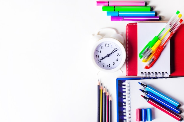 On a light surface, bright colorful stationery and a white alarm clock