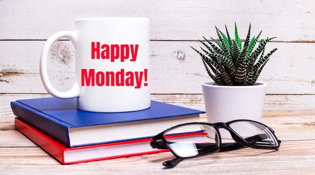 on a light table are notepads, a potted plant, black-framed glasses and a white cup with the text happy monday.