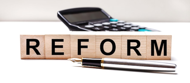 The light table has a black calculator a fountain pen and\
wooden cubes with the text reform business concept