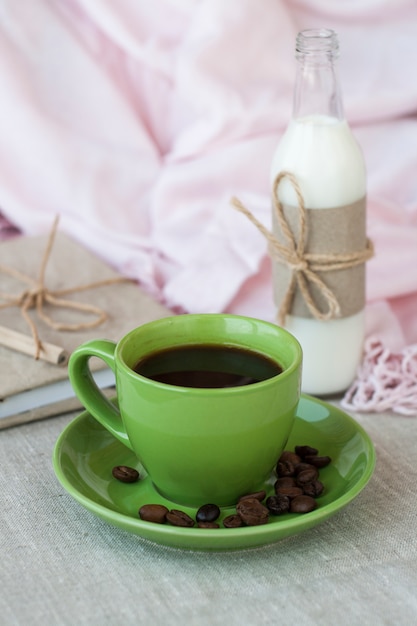 On a light table there is a cup of coffee and a bottle of milk. Next is a craft notebook and a pink napkin.