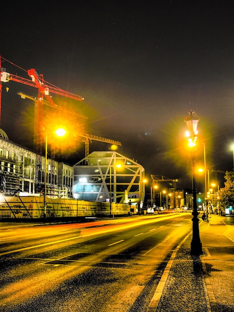 Light trail on city street by construction site against sky