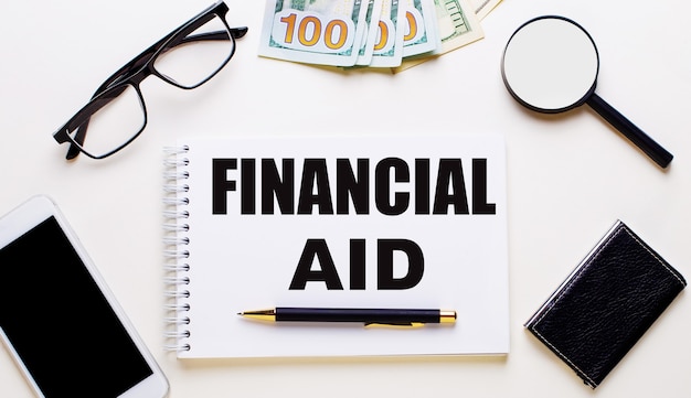 On a light wall, glasses, a magnifying glass, money, a phone and a notebook with the inscription FINANCIAL HELP. Business concept