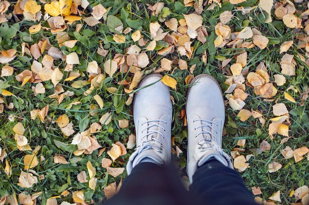 Light women shoes in autumn among green grass and orange leave