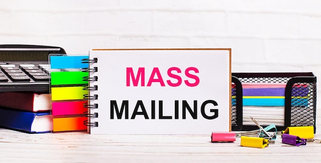 Su uno sfondo di legno chiaro una calcolatrice bastoni multicolore e un taccuino con il testo mass mailing business concept