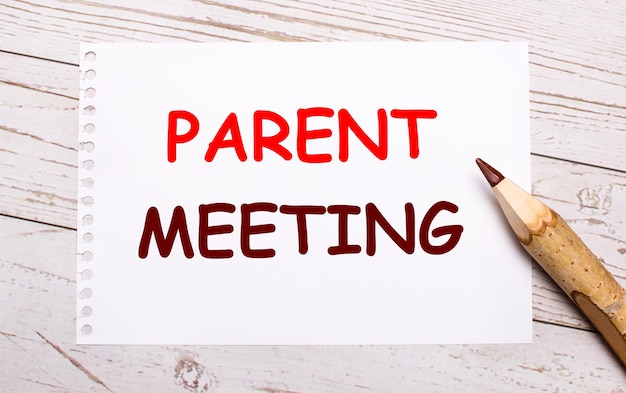 On a light wooden background, a colored pencil and a white sheet of paper with the text PARENT MEETING