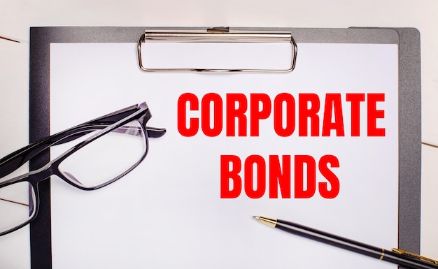 На светлом деревянном фоне очки, ручка и лист бумаги с текстом CORPORATE BONDS. Бизнес-концепция