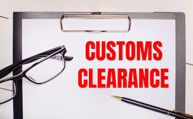 밝은 나무 배경 안경, 펜 및 CUSTOMS CLEARANCE라는 텍스트가 있는 종이. 비즈니스 개념