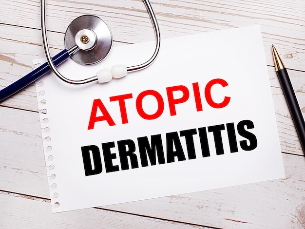 가벼운 나무 탁자에는 청진기, 펜, ATOPIC DERMATITIS Medical 개념이 적힌 종이 한 장이 있습니다.