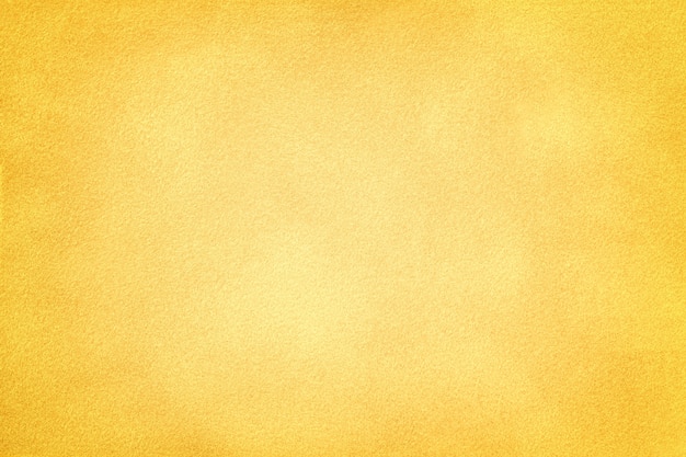 Light yellow matte background of suede fabric with dark vignette. Velvet texture of golden felt textile with gradient, macro.