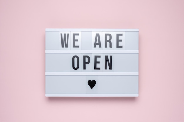 Lightbox met de tekst WE ARE OPEN op pastelroze achtergrond. Minimaal begrip.