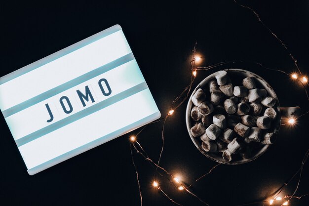 Lightbox met tekst JOMO Joy of Missing Out. Het concept van ontspanning van informatie en gadgets. Bovenaanzicht. Plat leggen. Beker met cacao en marshmallows. Digitale ontgifting