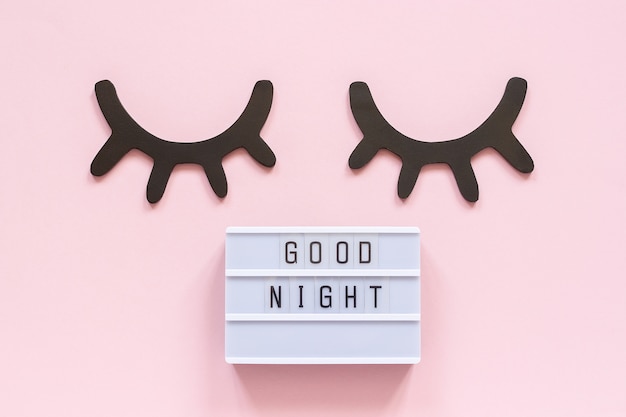 Lightbox-tekst Good Night en decoratieve houten zwarte wimpers, gesloten ogen op roze achtergrond.