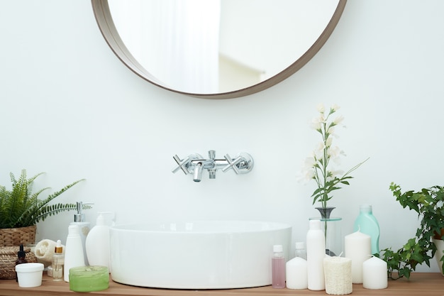 A lightcolored sink with mirror and tap next to the tubes of cream skin care cosmetics and face serums