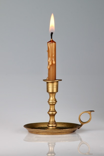 Lighted candle in an old brass candlestick, with a gray wall.