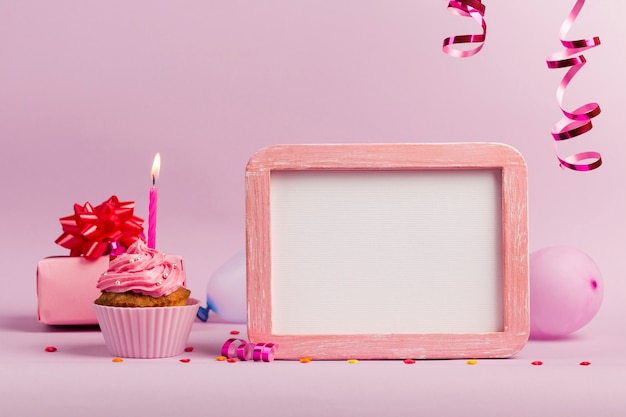 Photo lighted candles over the muffins with white frame slate on pink backdrop