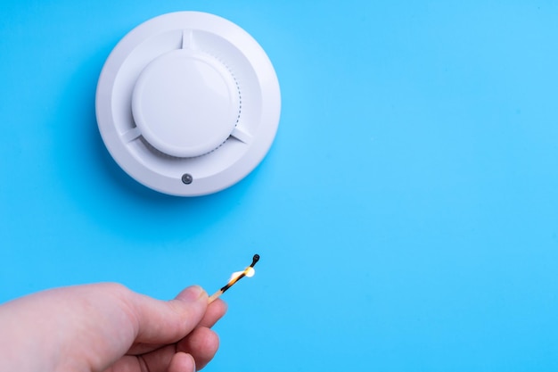 Lighted match in a woman's hand and a fire alarm on a blue
background. fire safety concept. copy-space