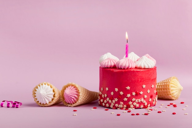 Candela numero uno accesa sulla deliziosa torta rossa con granelli di stelle e coni di cialda su sfondo viola