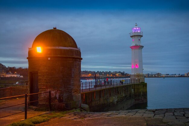 Lighthouse by building against sky during sunset