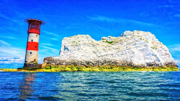 Lighthouse by sea against blue sky