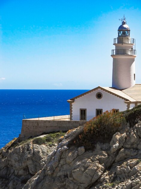 Lighthouse by sea against clear blue sky