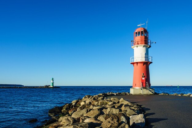 Lighthouse by sea against clear blue sky