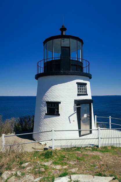 Lighthouse by sea against clear blue sky