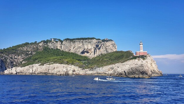 Lighthouse by sea against clear blue sky