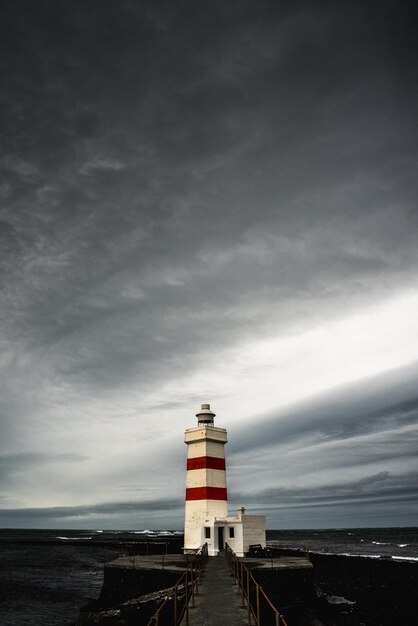 Photo lighthouse by sea against dramatic sky