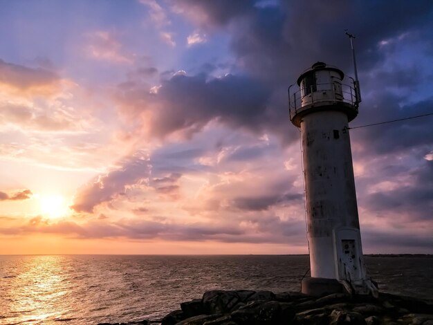 Lighthouse by sea against sky during sunset