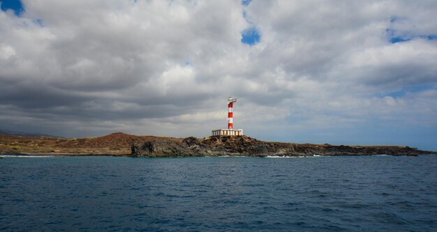 Lighthouse by sea and buildings against sky