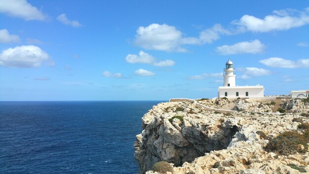 Lighthouse on cliff by sea against sky