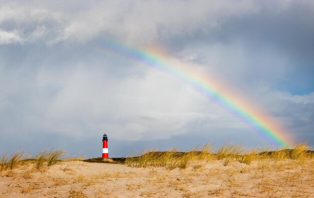 Lighthouse under rainbow at hornum sylt - rainy weather at dune landscape with special light