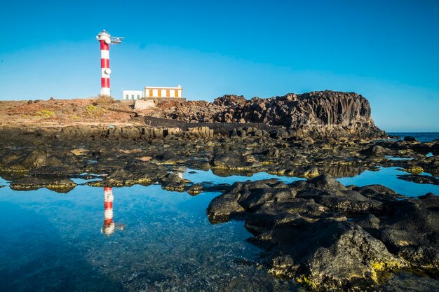 Lighthouse on rock by sea against sky