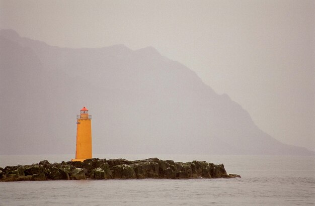 Foto faro sulle rocce contro la montagna durante il tempo nebbioso