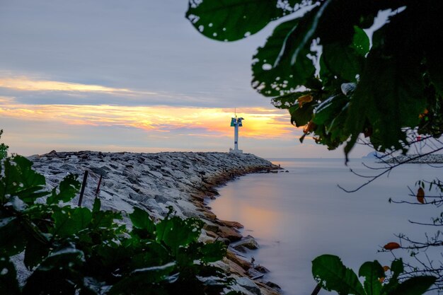 A lighthouse on the shore of a lake with the sun setting behind it.