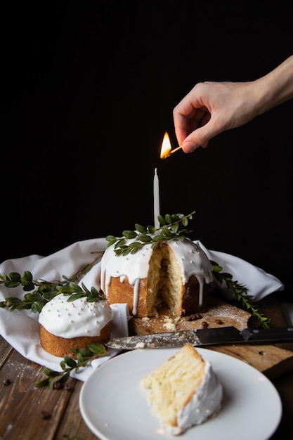 Lighting a candle on a glazed Easter cake a piece on a white plate on a dark background